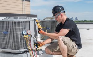 HVAC technician repairing wiring inside outdoor air conditioning unit during professional thermostat installation and HVAC repair service.